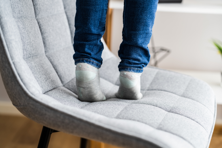 Close-Up von den Füßen eines kleines Kindes, das auf Zehenspitzen auf einem Sessel steht
