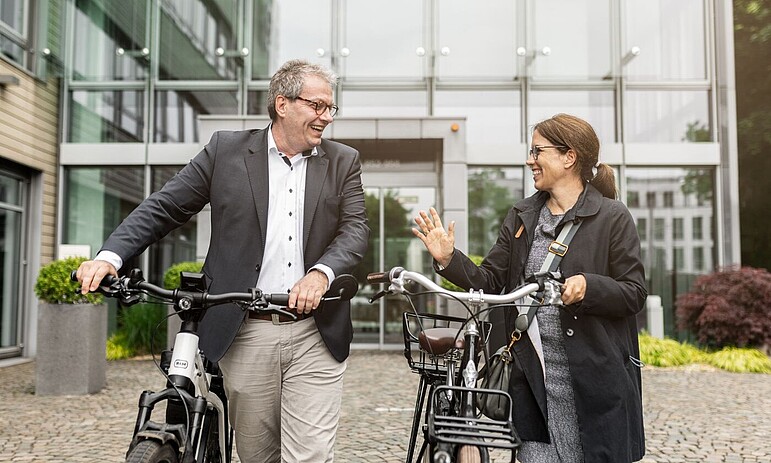 Zwei Mitarbeitende mit ihrem Jobrädern unterhalten sich lachend vor dem GVV Gebäude