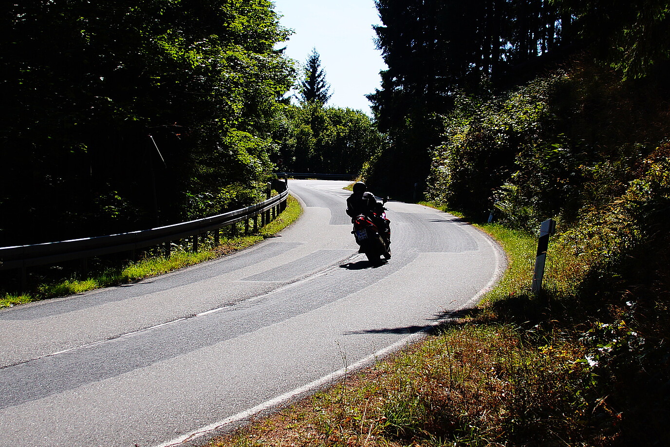 Eine motorradfahrende Person fährt eine kurvige Strecke im Harz entlang