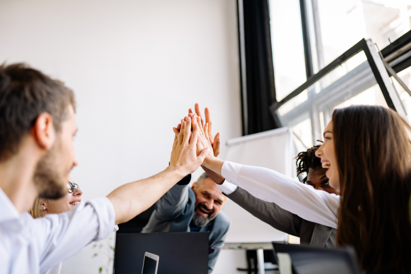 Drei Frauen und zwei Männer auf der Arbeit geben sich zufrieden einen High Figh