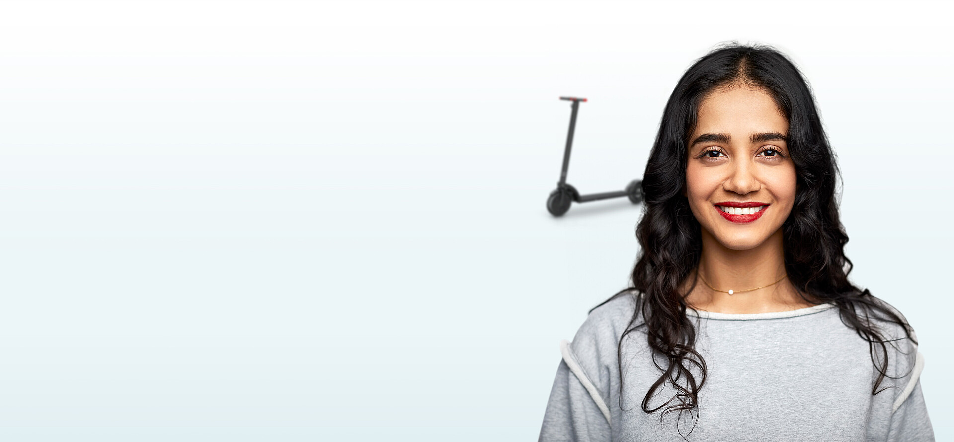 Junge lächelnde Frau mit einem E-scooter im Hintergrund