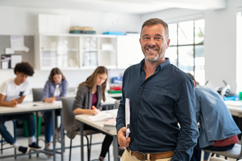 Lehrer lächelt in einem vollen Klassenraum in die Kamera