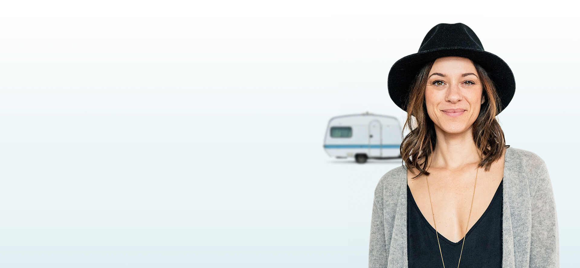 Lächelnde Frau mit Hut und einem Wohnwagen im Hintergrund