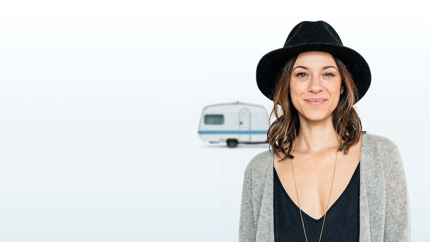 Lächelnde Frau mit Hut und einem Wohnwagen im Hintergrund
