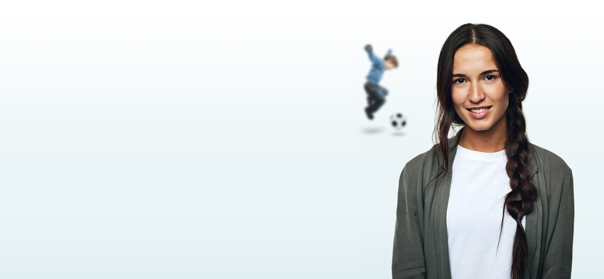 Geschäftsfrau mit geflochtenen Haaren mit einem Fußball spielendem Kind im Hintergrund