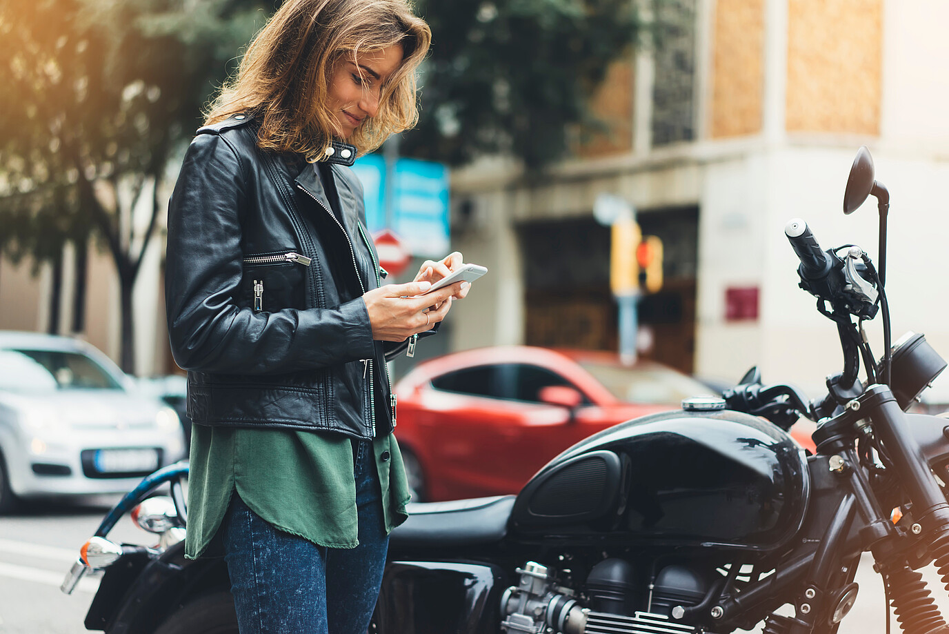 Eine Frau steht vor ihrem Motorrad und schaut auf ihr Handy