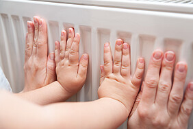 Die Hände von einem Erwachsenen und einem Baby fühlen, wie warm die Heizung ist. 
