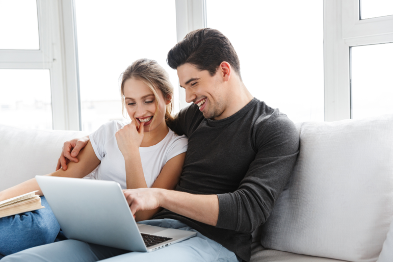 Ein Mann und eine Frau sitzen auf dem Sofa lächelnd vor einem Laptop