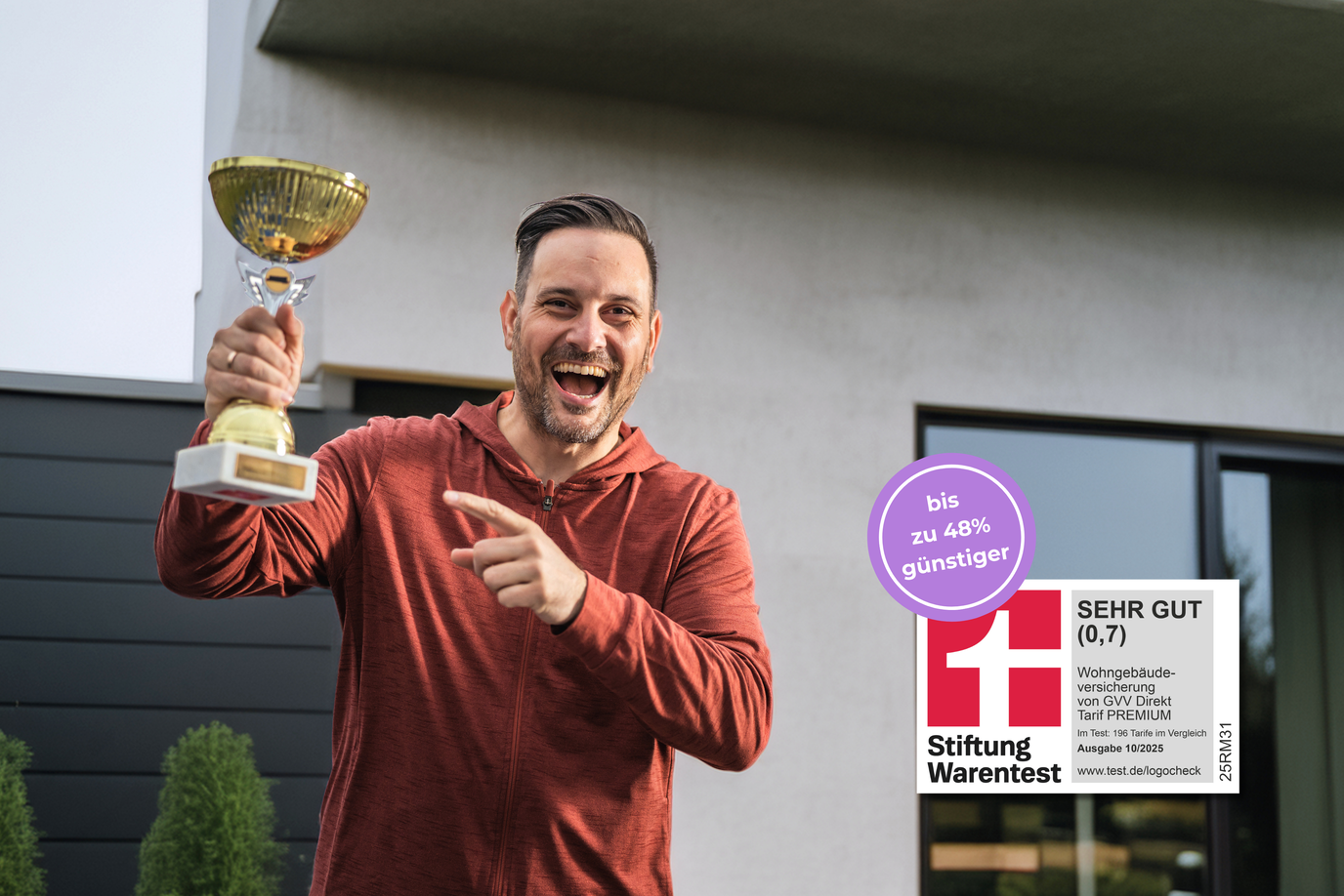 Ein Mann steht jubelnd vor seinem Haus und hält einen Pokal in die Luft