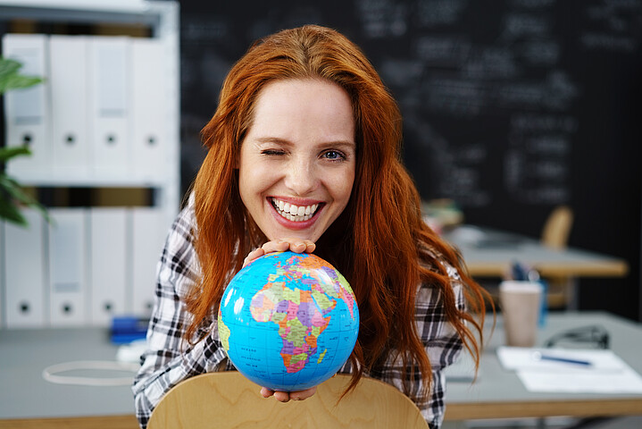 Eine junge Frau lächelt und hält einen Globus in der Hand. 