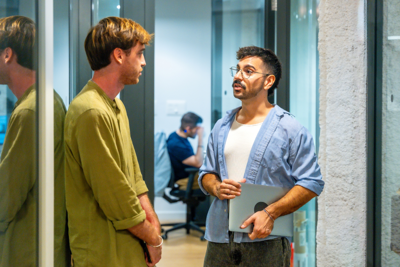 Zwei junge Männer im Büroflur stehen sich gegenüber und unterhalten sich