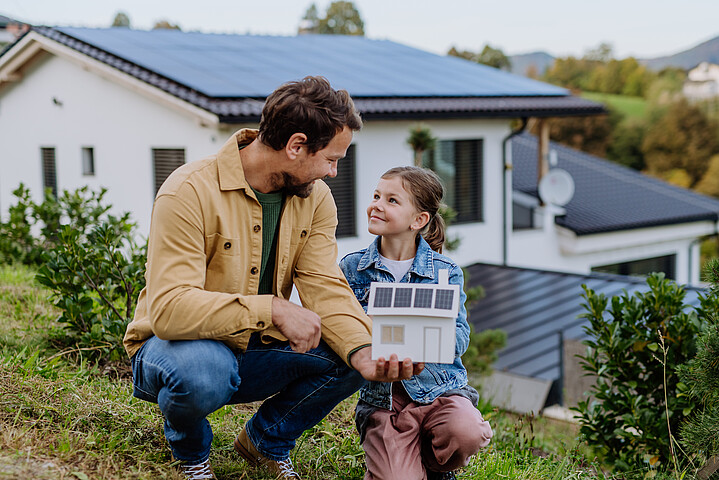 Vater und Tochter stehen vor ihrem Haus, das eine Photovoltaikanlage auf dem Dach hat