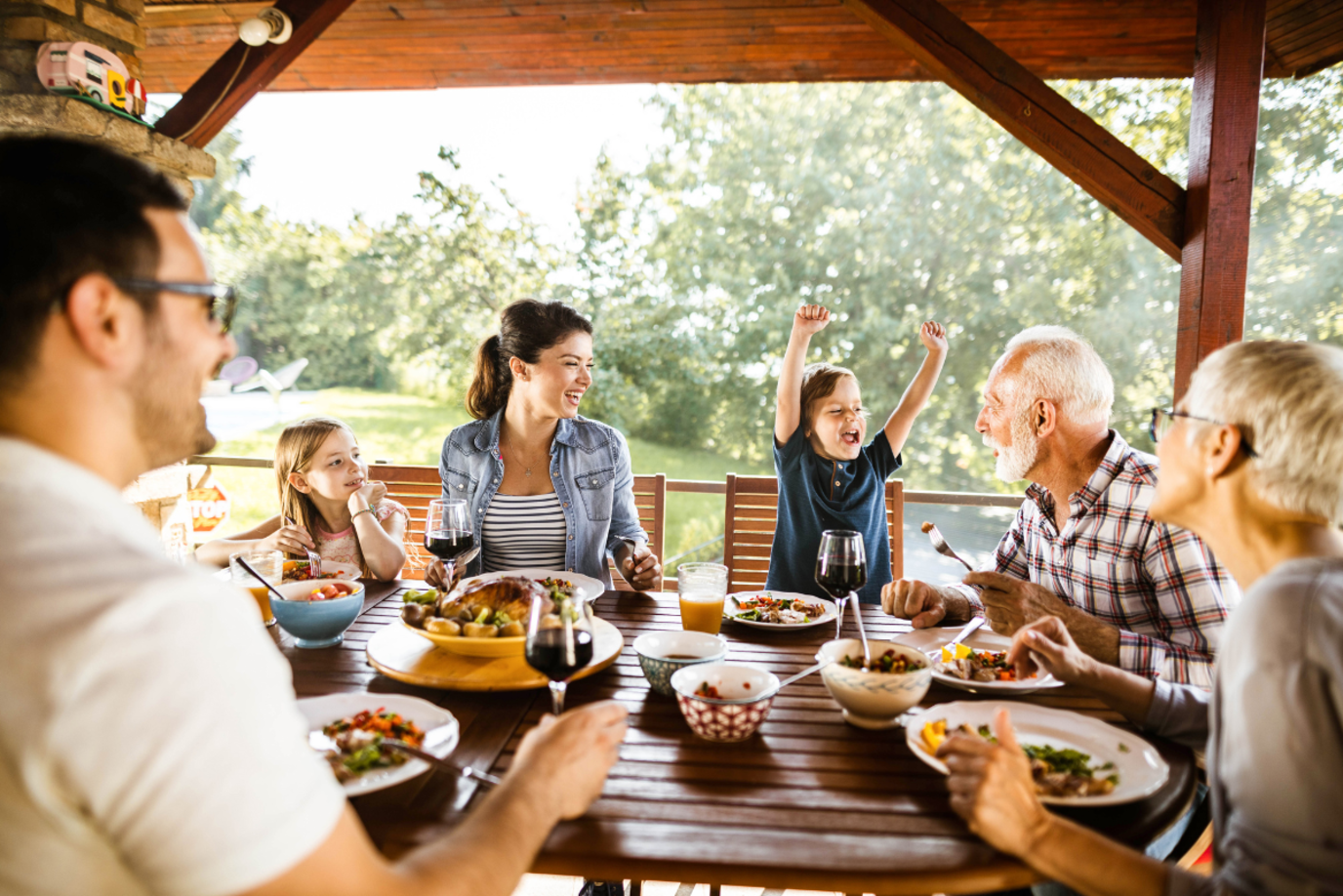 Große Familie, bestehend aus Opa, Oma, Mutter, Vater und zwei kleinen Kindern, isst im Garten unter einem Dach