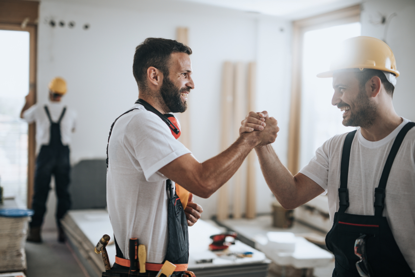 Zwei Männer auf einer Baustelle geben sich im Haus zufrieden einen Handschlag