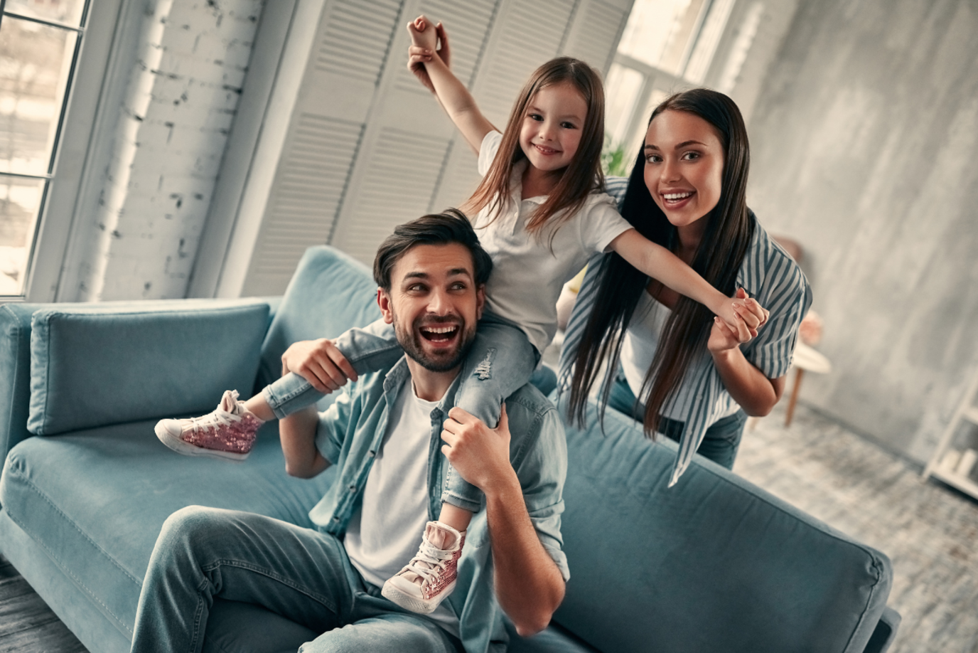 Mutter, Vater und Tochter sitzen auf dem Sofa im Wohnzimmer und jubeln