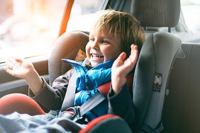 Ein kleines Kind sitzt im Auto im Kindersitz und freut sich