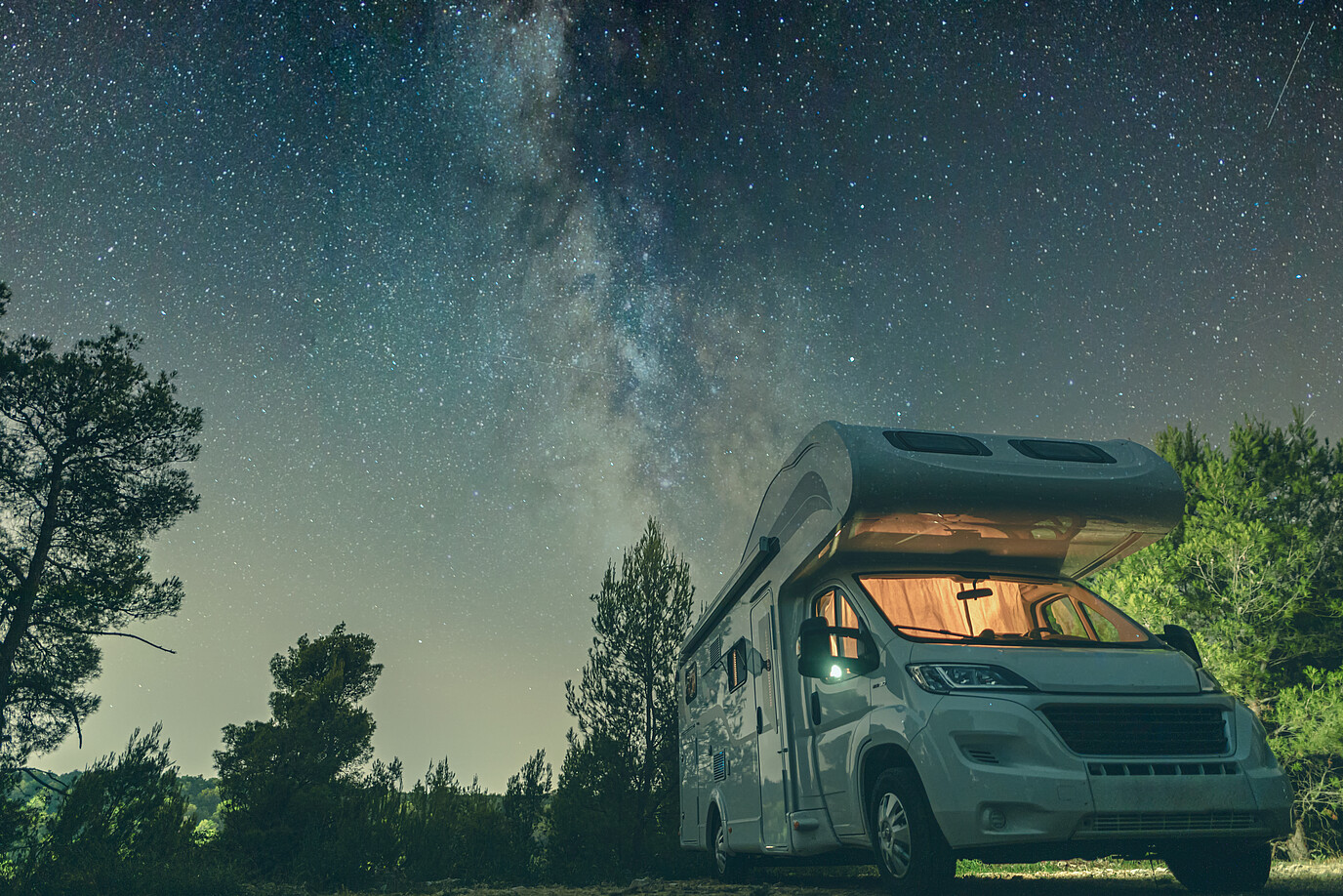 Ein Wohnmobil steht bei Nacht unter einem Sternenhimmel