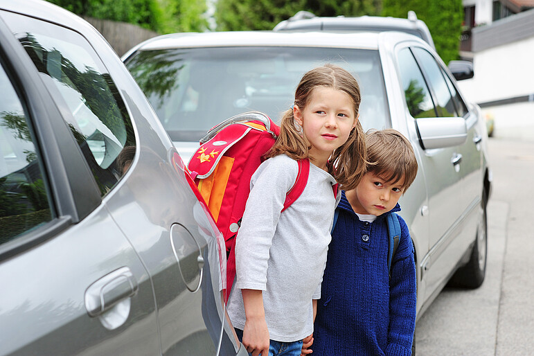 Zwei Schulkinder wollen die Straße überqueren und stehen zwischen zwei Autos
