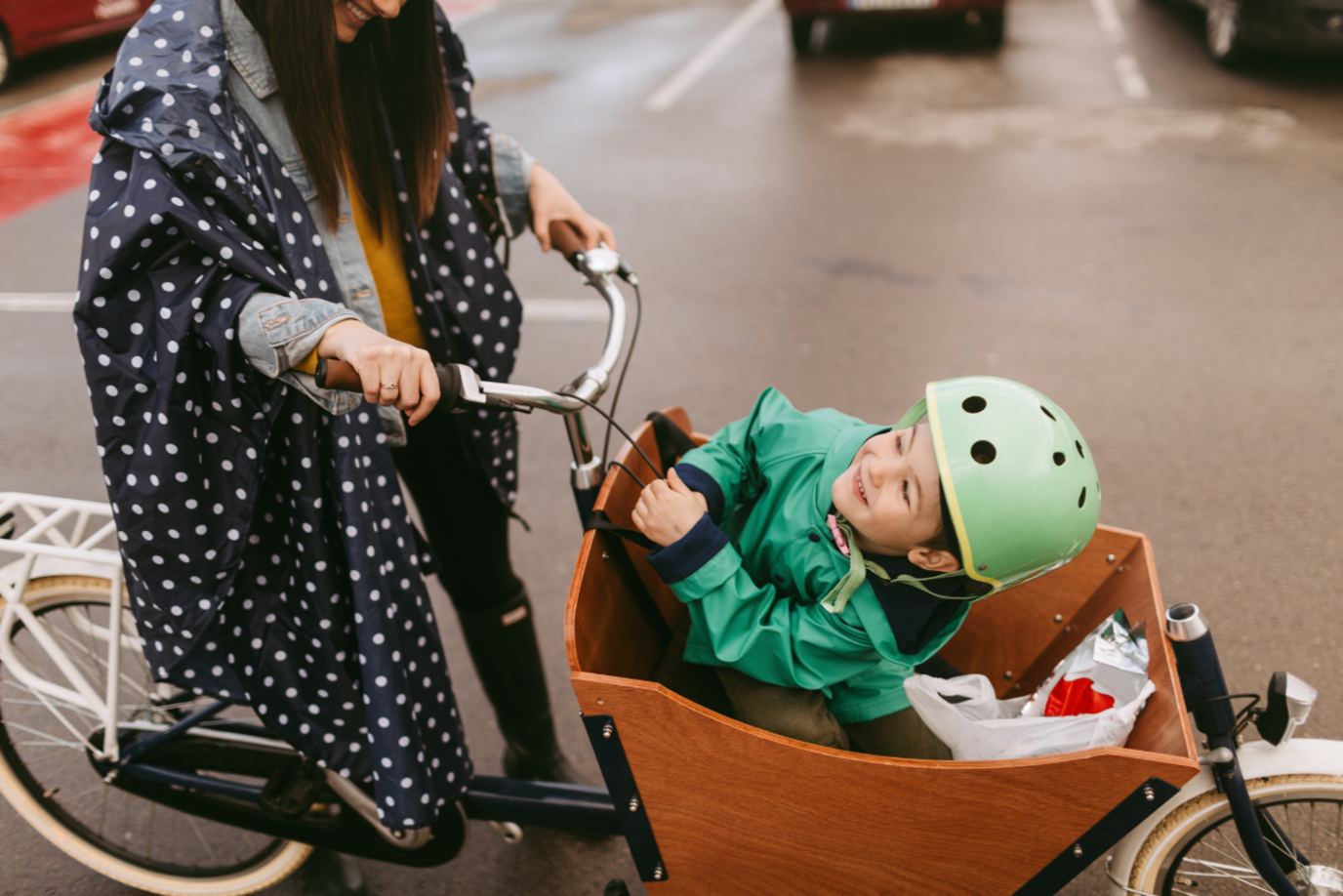 Kind und Mutter auf dem Lastenrad stehen auf einem Parkplatz und lächeln sich an