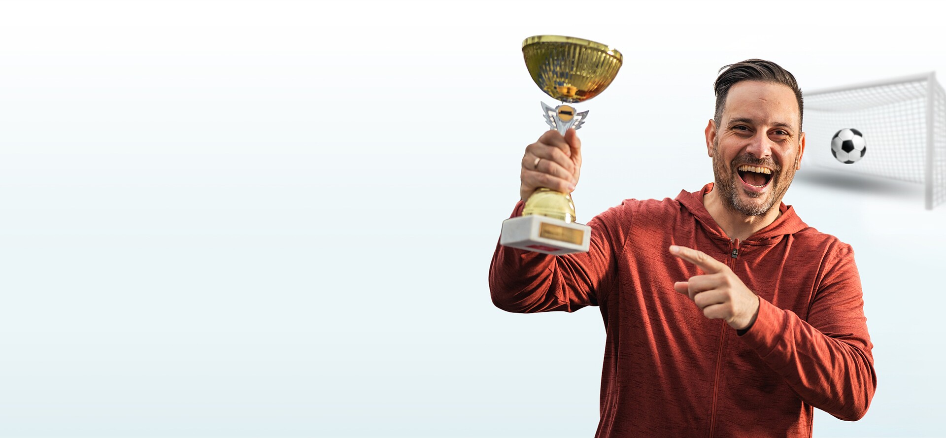 Ein junger Mann hält jubelnd einen Pokal in der Hand und zeigt auf ihn