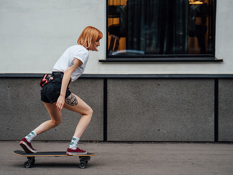 Junge Frau fährt ein Carver Skateboard auf dem Bürgersteig
