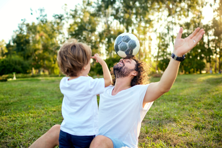 Vater und Sohn sitzen im Gras und spielen mit einem kleinen Ball