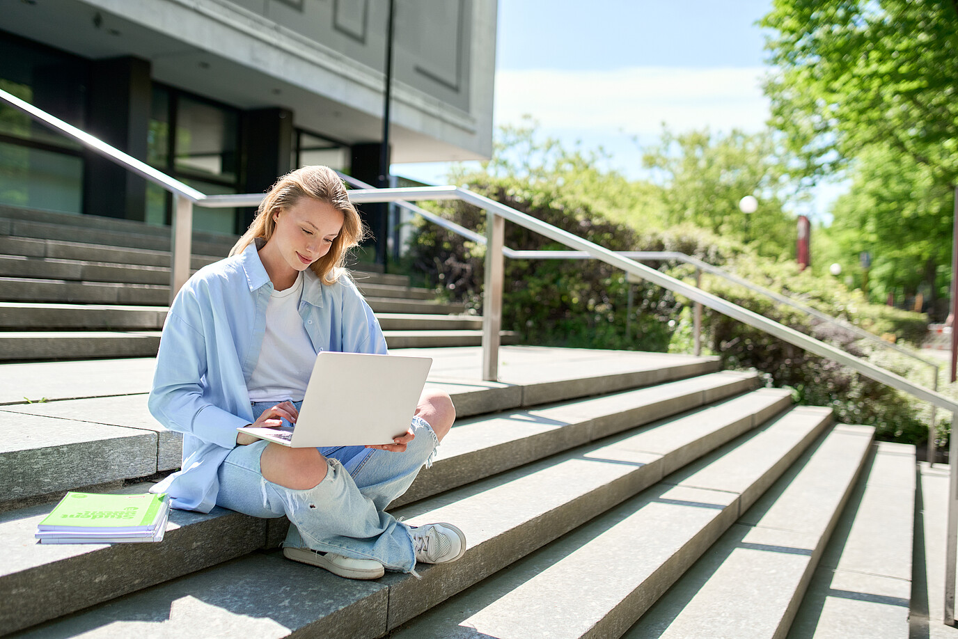 Eine junge Studentin sitzt auf einer Treppe und arbeitet am Laptop. 