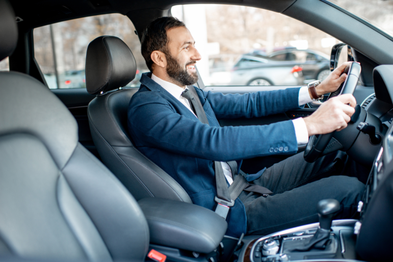 Mann im Anzug fährt lächelnd Auto