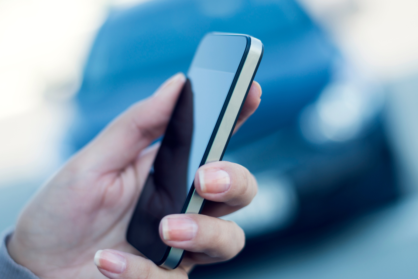 Close-Up von einer Hand mit einem Handy und im Hintergrund ein verschwommenes Auto