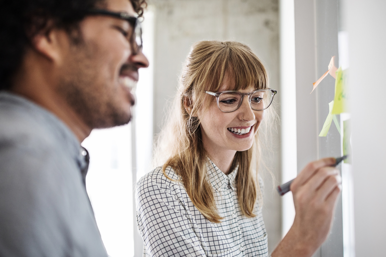 Zwei Menschen arbeiten lächelnd an einem Whiteboard im Büro zur Ideen-Findung