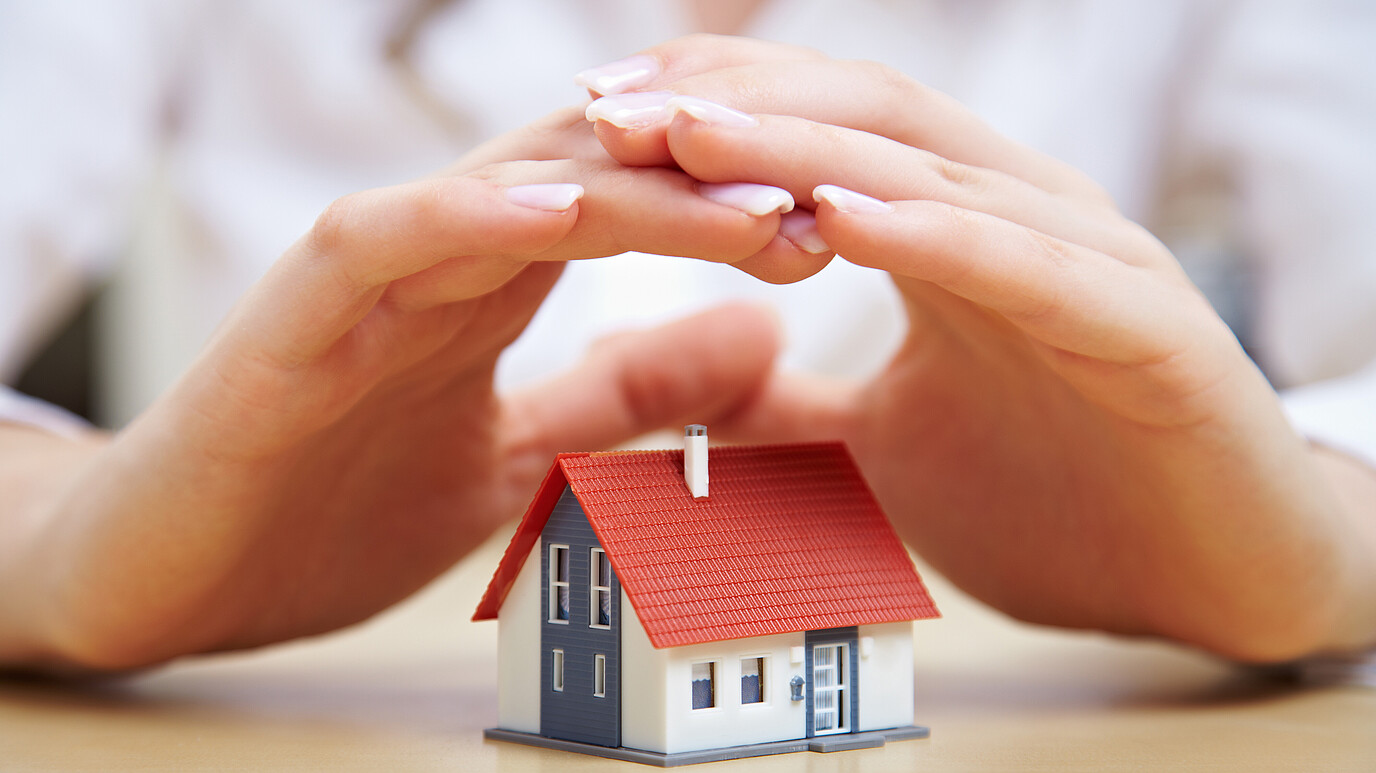 Hände schützen ein Miniaturhaus