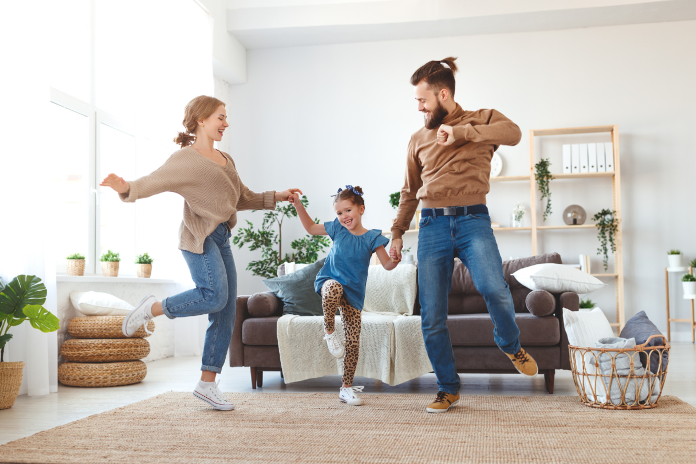 Familie aus junger Mutter und jungem Vater und kleiner Tochter tanzt und springt glücklich im Wohnzimmer