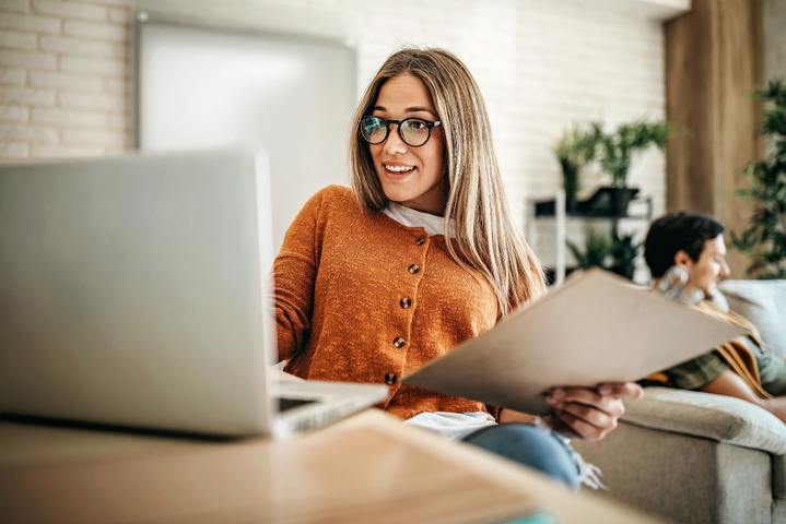 Junge Frau sitzt lachend am Laptop und arbeitet