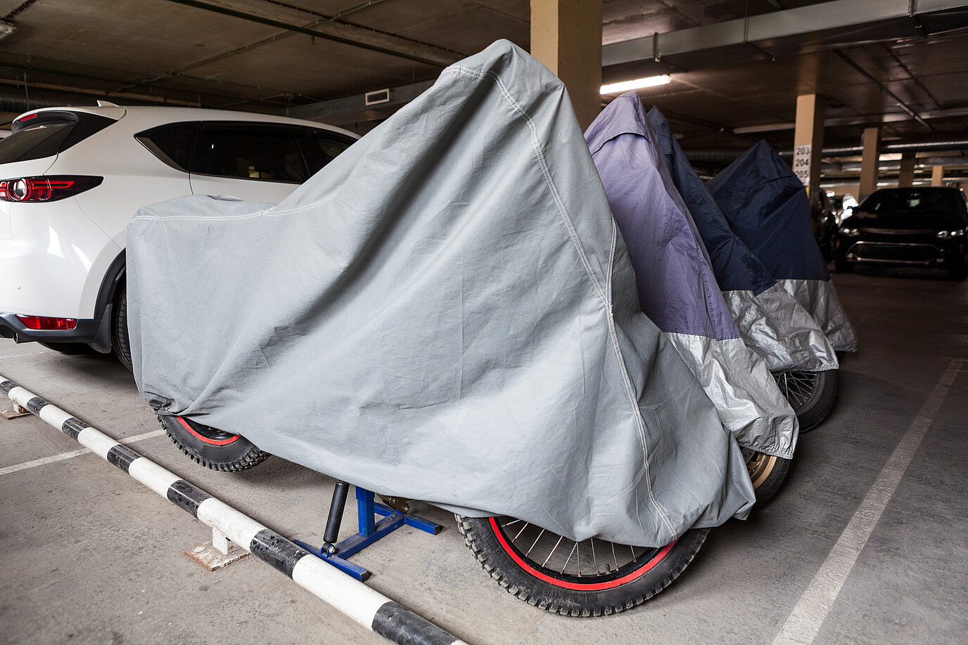 Motorräder stehen mit einer Plane abgedeckt in einer Garage