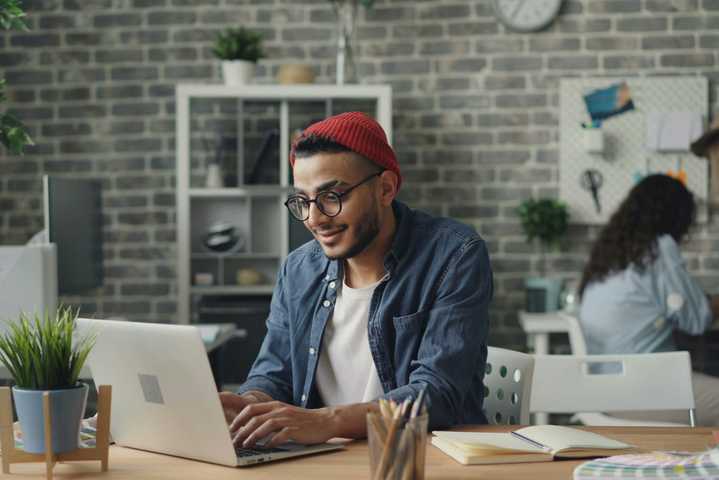 Junger Mann sitzt zufrieden am Laptop und tippt