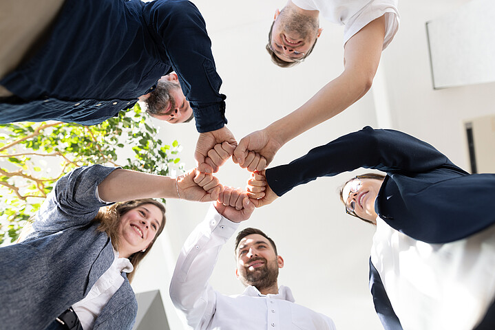 Zwei Frauen und drei Männer stehen im Kreis und geben sich die Faust, um Teamgeist zu zeigen