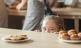 Kleines Mädchen schaut Süßwaren an, die auf dem Tisch stehen