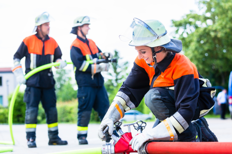 Feuerwehrfrau im Einsatz scheibt den Wasserschlauch zusammen