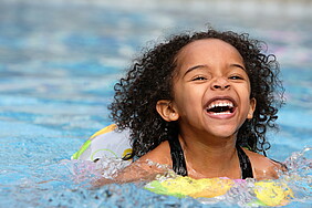 Ein Kind schwimmt vergnügt im Wasser mit einer Schwimmhilfe