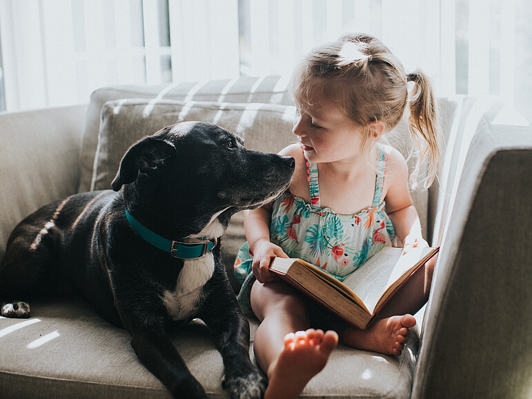 Kleines süßes Mädchen liest ein Buch mit ihrem Hund