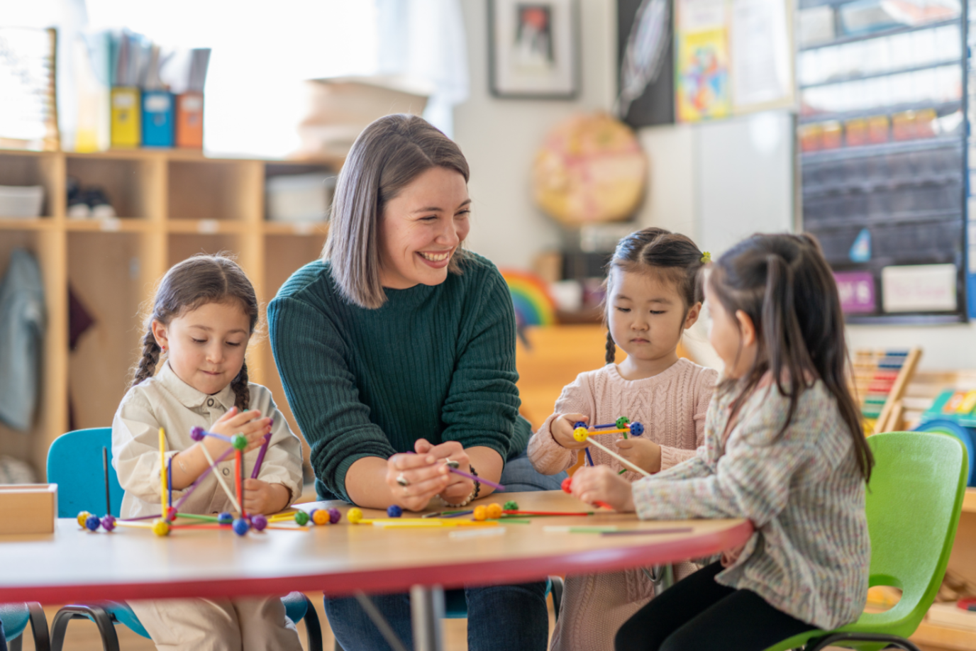 Grundschullehrerin sitzt mit drei kleinen Kindern lachend in der Klasse
