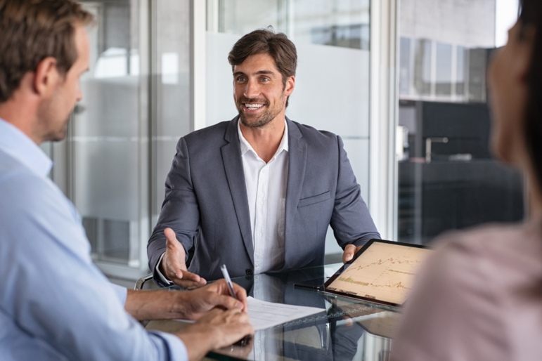 Mann im Anzug berät zwei Personen am Schreibtisch zum Thema Finanzen