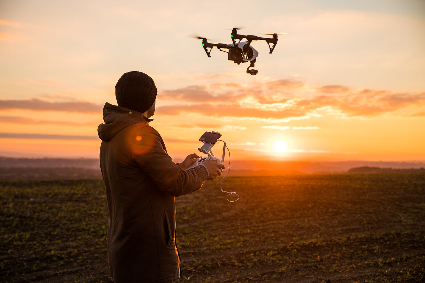 Eine Person steuert eine Drohne vor dem Sonnenuntergang. 