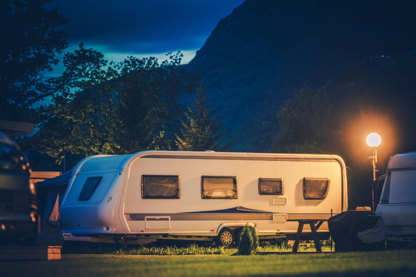 Beleuchteter Wohnwagen bei Nacht auf dem Campingplatz in den Bergen