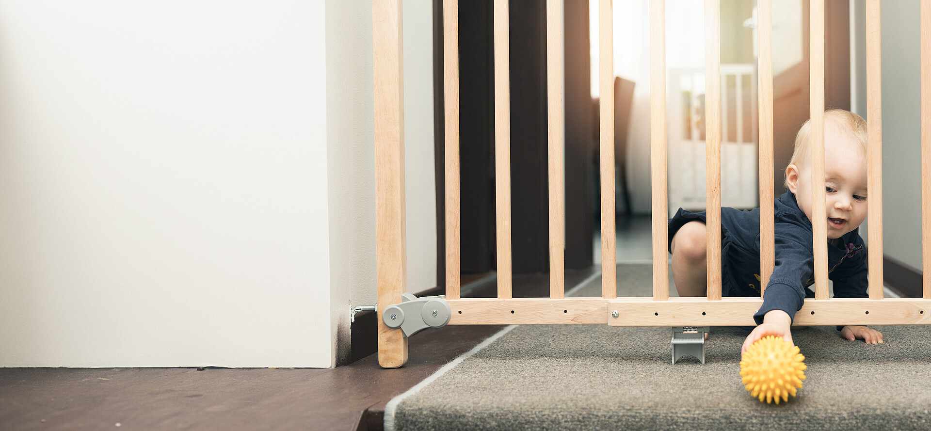 Baby greift durch ein Sicherheitsgitter in der Wohnung und spielt mit einem Ball