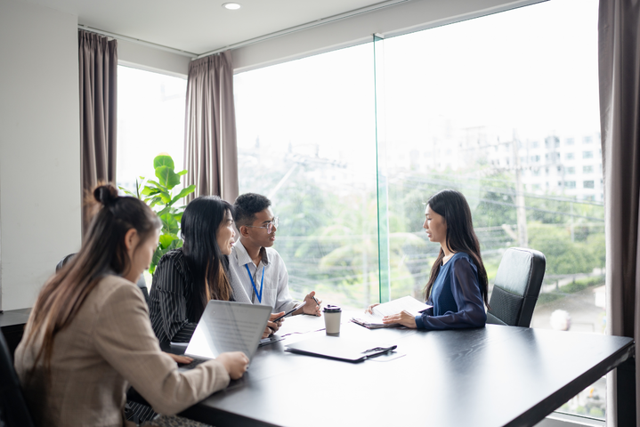 Eine Frau sitzt drei Personen in einem Vorstellungsgespräch an einem Tisch gegenüber