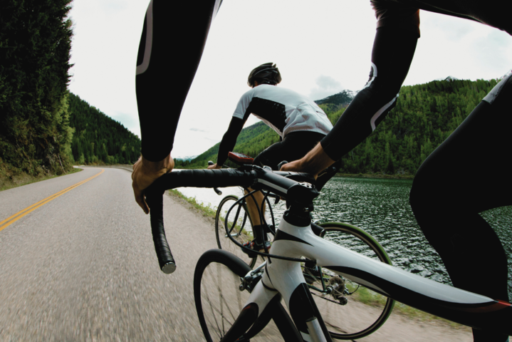 Zwei Rennradfahrer von hinten auf einer Straße am See