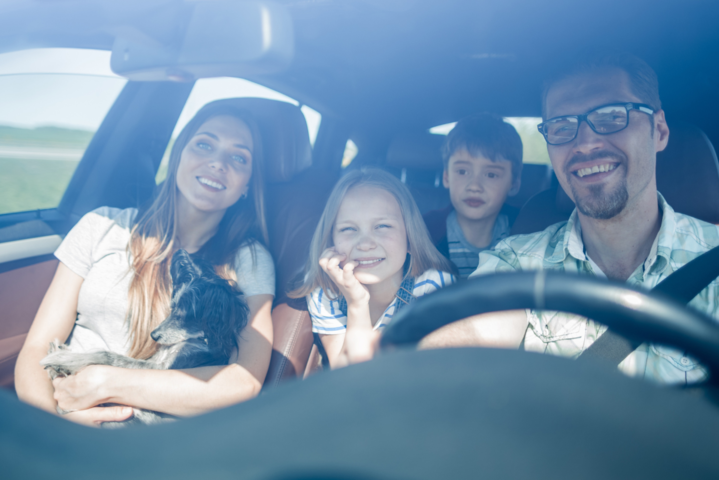 Mann, Frau und zwei kleine Kinder sitzen im Auto und sind glücklich