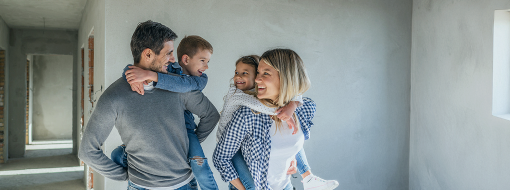 Eltern mit ihren zwei Kindern auf dem Rücken gehen glücklich durch eine Baustelle.