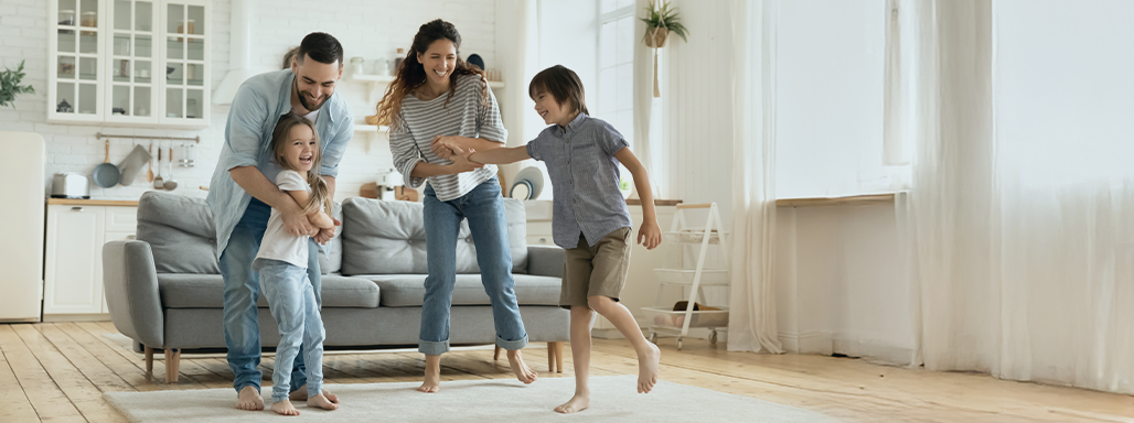 Eine junge Familie mit zwei Kindern spielt glücklich in ihrem Wohnzimmer.